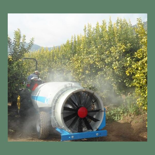 Una pulverizadora agrícola grande, arrastrada por un tractor, aplicando una fina niebla en un huerto de árboles frutales verdes. Se aprecia la maquinaria en acción, con el ventilador principal visible en la parte frontal.